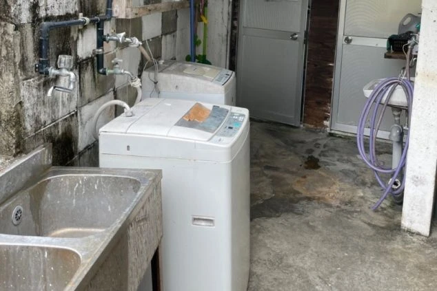 寮の共同ランドリー。屋外に洗濯機とシンクが設置され、生活感が漂う。