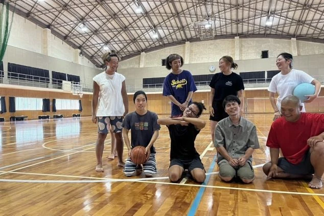 体育館で楽しそうに集まる男女グループ。バスケットボールを片手に、皆笑顔でポーズをとっている。