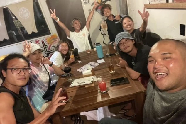 飲食店で食事をする友人たち。皆笑顔で、お酒やドリンクを片手にポーズをとっている。