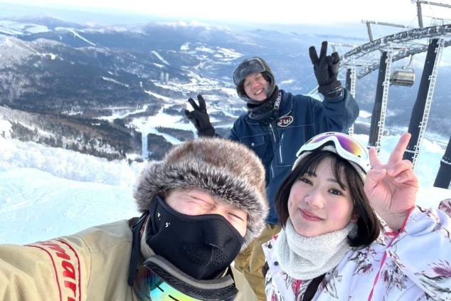 雪山を背景に、若い男女3人が笑顔でポーズを取っている画像。リゾートバイトの休日に仲間とスノボを楽しむイメージ。
