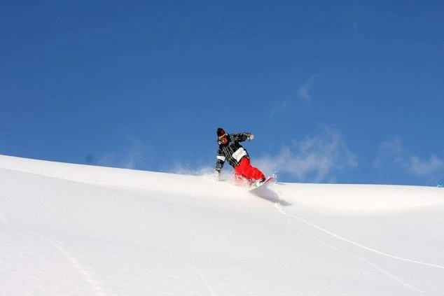 青い空の下、白いゲレンデでスノーボードを楽しむ人物。冬のリゾートバイトで、スキー場スタッフとして働きながらウィンタースポーツを満喫できることを示す画像。