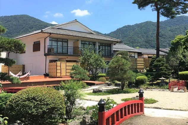 格式高いリゾートバイト先の温泉旅館の庭園。赤い橋と竹垣が配され、奥には山々が広がる。