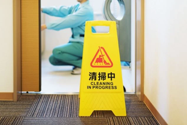  清掃中の看板が置かれた廊下。その奥で、制服を着たスタッフが清掃作業をしている様子。