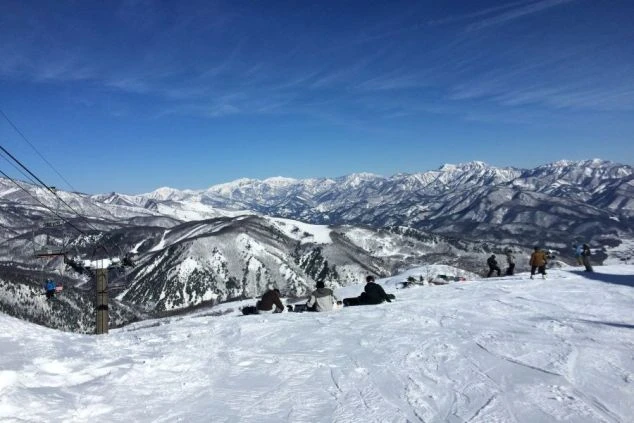 雪に覆われたゲレンデに座る人々。眼下に広がる街並みと山々を眺める絶景のイメージ画像。リゾートバイトの休日を満喫。