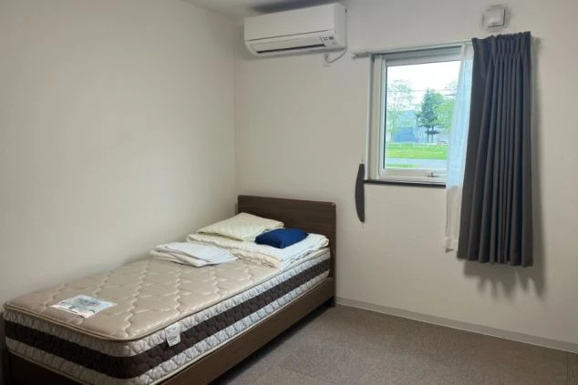 リゾートバイトの寮の個室。ベッドとエアコンが完備された、シンプルで清潔感のあるプライベート空間。
