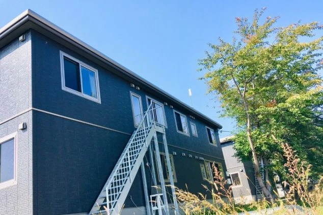 寮の外観。紺色の壁と白い外階段を持つ2階建ての建物が映る。	