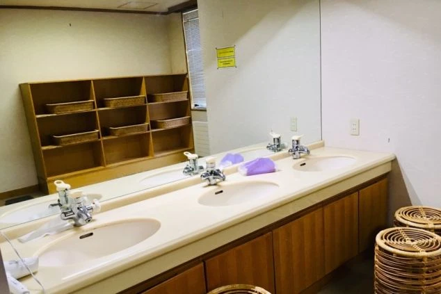 寮の共用洗面台。複数のシンクと鏡、カゴ付きの収納棚が映る。