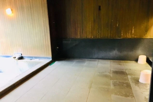 寮のお風呂。湯が張られた浴槽と、木板の壁が映る共同浴場。