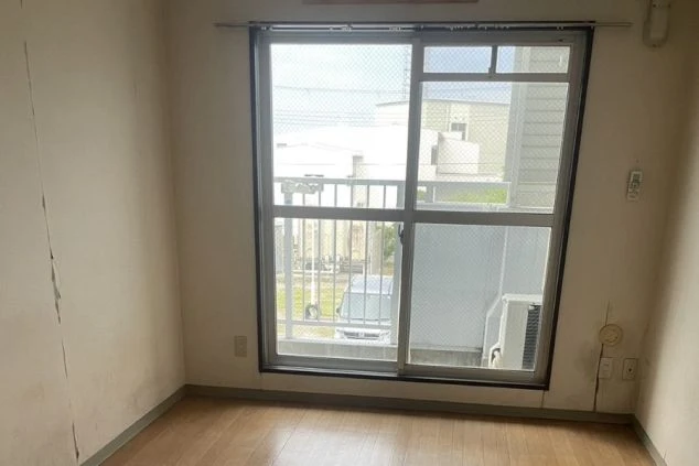 リゾートバイトの寮の個室。フローリングの部屋に、ベランダへ通じる大きな窓があり、日当たりが良い。