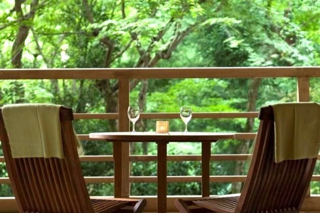 ホテルのバルコニー。緑豊かな森を背景に、テーブルと椅子、ワイングラスが並ぶ落ち着いた空間が映るイメージ画像。リゾートバイトの休日を満喫。