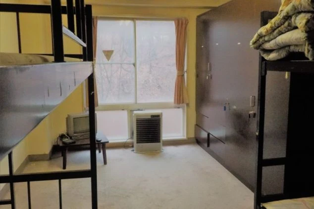 寮の相部屋。二段ベッド、クローゼット、テレビ、暖房器具が映る。