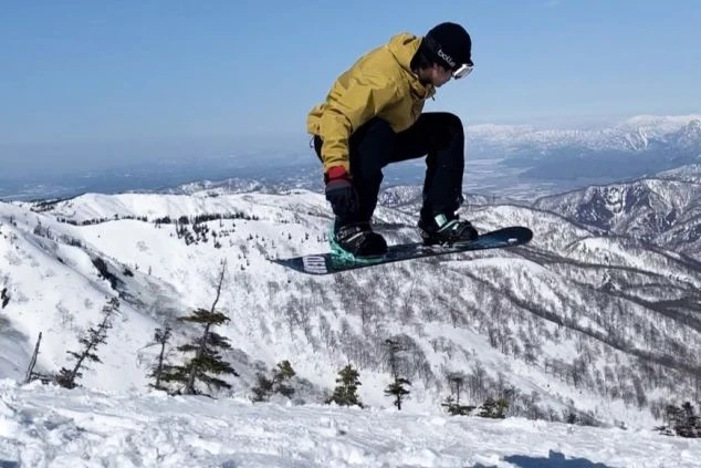 スノーボードでジャンプする様子。雪と山が広がるゲレンデが映るイメージ画像。リゾートバイトの休日を満喫。