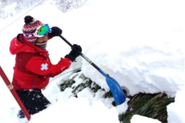 雪山でスコップを使い雪を掘る人物が映るイメージ画像。リゾートバイトの業務の様子。