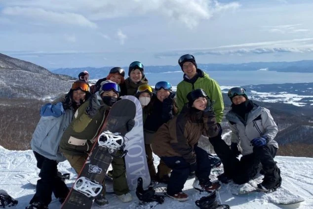 ワクトリでリゾートバイトをしたスタッフが撮影した、雪山の山頂で大勢の仲間がスノーボードとスキーを持って笑顔で並ぶイメージ画像。リゾートバイトの休日を満喫。