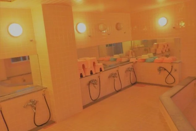 寮の大浴場。シャワーと鏡、椅子、湯船が並ぶ広々とした浴室が映る。