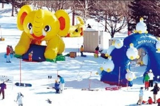 スキー場のキッズパーク。雪のゲレンデに象の巨大なバルーンや遊具が設置された様子が映るイメージ画像。リゾートバイトの休日を満喫。