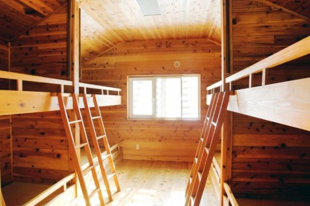 リゾートバイトの相部屋寮の室内。木の温もりが感じられる広々とした空間に、二段ベッドが複数台設置されています。共同生活を楽しみたい方におすすめです。