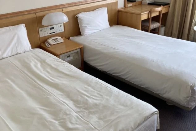 リゾートバイトの相部屋寮の寝室。ホテルタイプの客室で、清潔なツインベッドとデスクが備え付けられており、快適なプライベート空間で過ごせます。