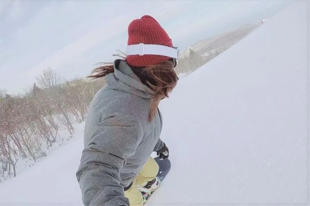 雪山で、スノーボードで滑走している女性の画像。リゾートバイトの休日にスノボを楽しむイメージ。