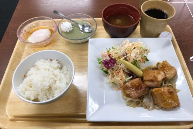 唐揚げのような肉料理、ご飯、味噌汁、サラダ、デザート、コーヒーが乗った定食。