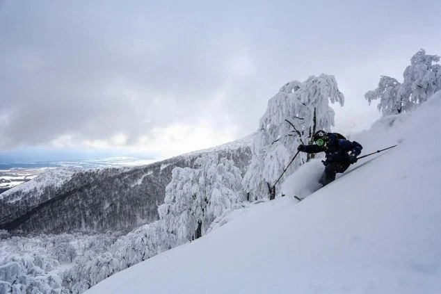 青空の下、雪山を背景にスノーボードをする2人の画像。リゾートバイトの休日に仲間とウィンタースポーツを楽しむイメージ