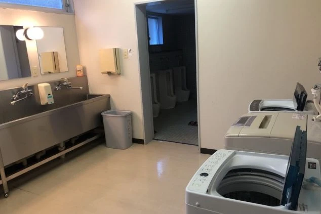 リゾートバイトの寮の水回りの画像。共同の洗面台と洗濯機、奥にはトイレが見える。