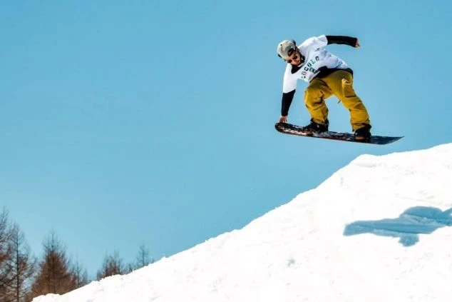 青空の下、スノーボードでジャンプする人。スキー場やスノーボード場で働くリゾートバイトのイメージ画像。