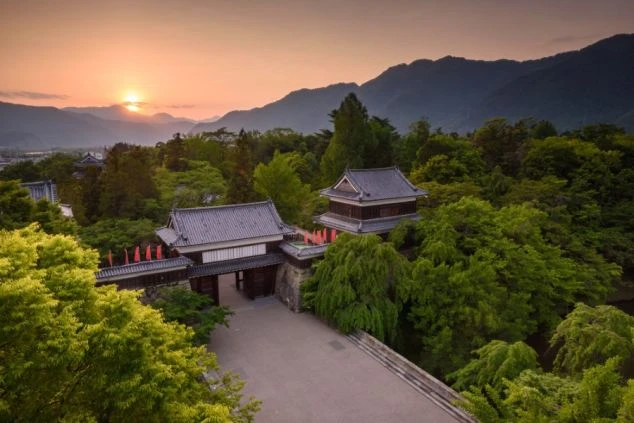 夕焼けに照らされた長野県の上田城跡公園。門や櫓が緑の木々に囲まれ、歴史と自然が調和した場所でのリゾートバイトに興味がある方に魅力的な画像。