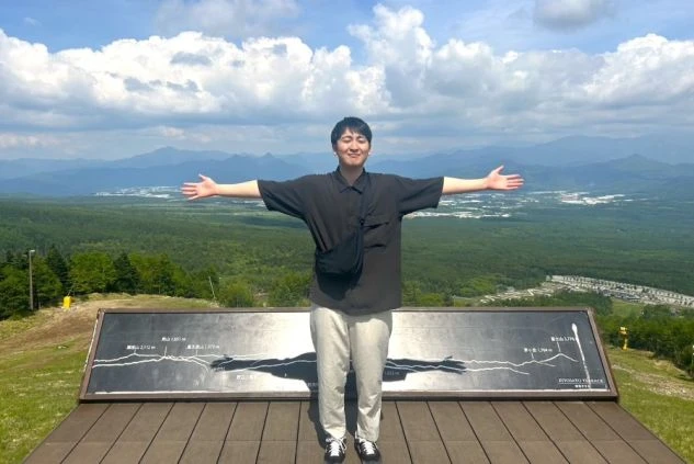 広大な高原の絶景を背景に、両手を広げて立つ男性。リゾートバイトの仕事の後に、自然の中でリフレッシュしたい方に魅力が伝わるワクトリスタッフが撮影したオリジナル画像。