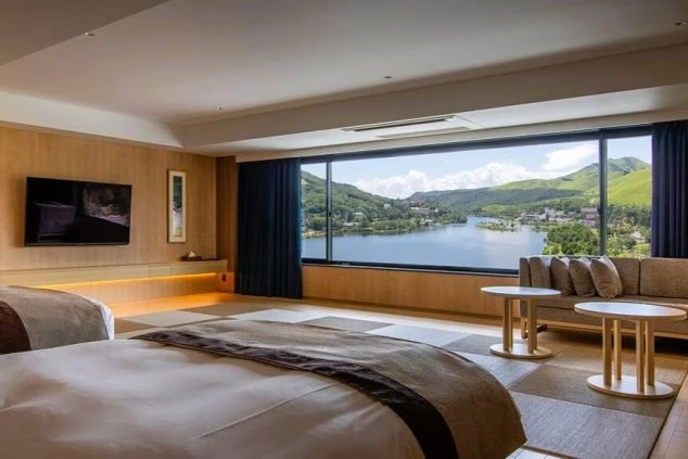 白樺湖の絶景が一望できる、広々としたリゾートホテルの客室。和洋室タイプで、ベッドとソファが置かれ、リゾートバイトで働く場所のイメージが伝わる画像。