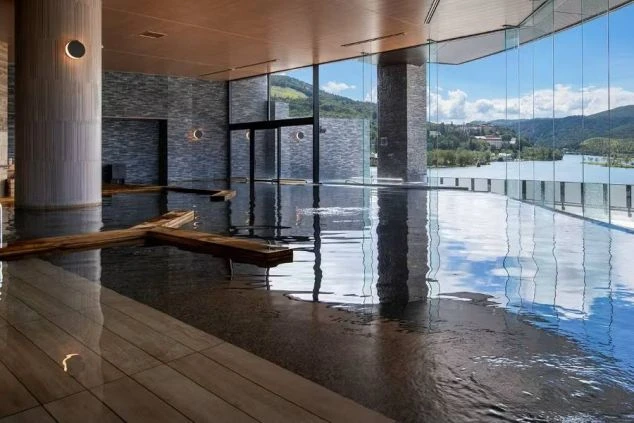 白樺湖の絶景が一望できる、リゾートホテルの内風呂。窓から光が差し込み、水面には空が反射している、リゾートバイトで温泉地での仕事と癒やしを両立したい方に魅力的な画像。