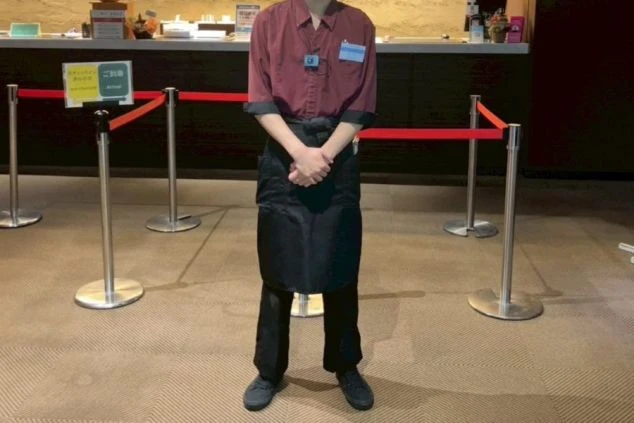 レストランで働く男性スタッフ。バーガンディ色のシャツに黒いパンツとエプロンを着用。落ち着いた色合いの制服で、仕事の雰囲気を伝える。