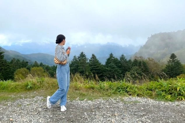 霧が立ち込める山と森を背景に、自然の中で佇む女性の後ろ姿。リゾートバイトで、仕事の合間に大自然を満喫し、リフレッシュしたい方に魅力的なワクトリスタッフが撮影したオリジナル画像。