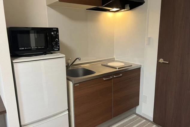 リゾートバイトの寮の個室にあるキッチン。IHコンロ、シンク、冷蔵庫、電子レンジがコンパクトにまとまっている。