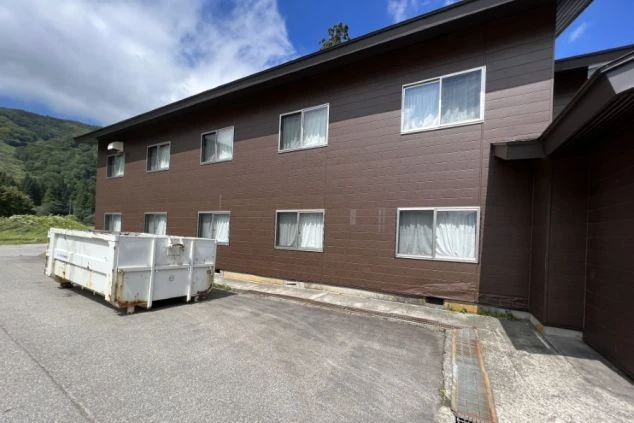 リゾートバイトの住み込み寮の外観写真。茶色い壁の2階建て集合住宅。豊かな自然に囲まれた立地。