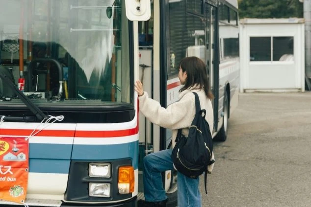 スキーリゾートの無料送迎バスに乗る女性。バックパックを背負い、これから出かける楽しそうな様子。
