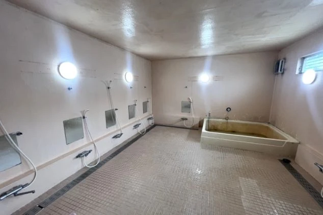 リゾートバイト寮の共用大浴場。シャワーブースが複数並び、湯船も見える、仕事の疲れを癒せる設備の画像。