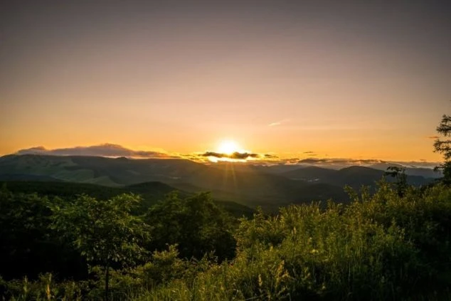 山々の間に沈む夕日と、光に照らされる緑の木々。リゾートバイトで、仕事の後に美しい夕焼けを眺めてリフレッシュしたい方に魅力的な画像。