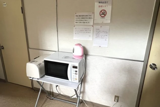 リゾートバイト寮の共用部に置かれた電子レンジと電気ケトル。壁には掲示物があり、寮のルールや生活の様子が伝わる画像の寮画像。