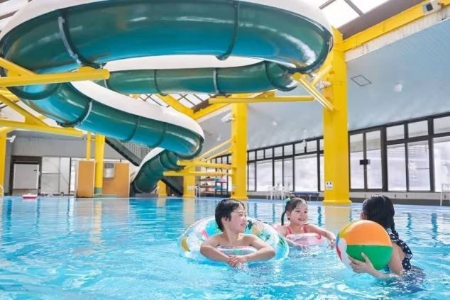 ウォータースライダーがある室内プールで、楽しそうに遊ぶ子供たち。リゾートバイトでホテルのプール監視員やレジャー施設のスタッフとして働くイメージが伝わる画像。