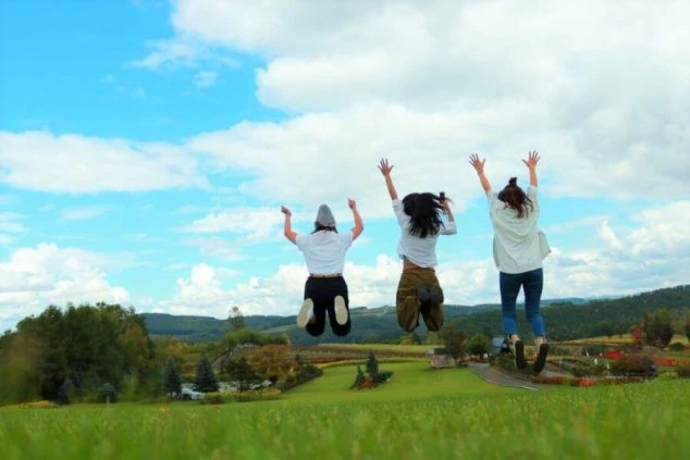 広大な高原で、楽しそうにジャンプする3人の女性の後ろ姿。リゾートバイトで出会った仲間と、仕事の休日に自然を満喫している様子が伝わるワクトリオリジナル画像。