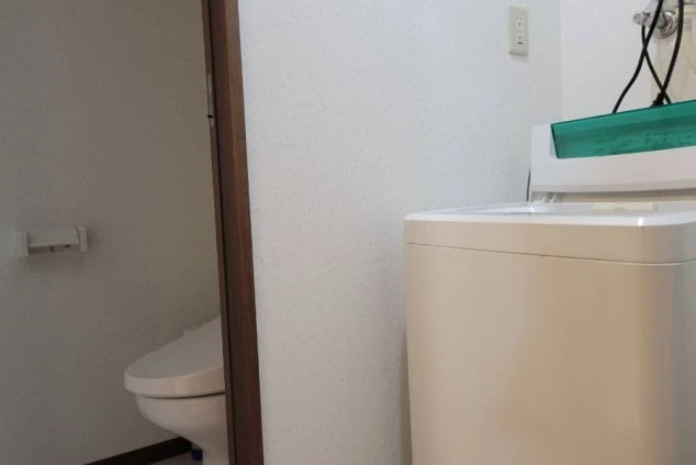 寮のランドリー。洗濯機とトイレが見える共用スペースが映る。