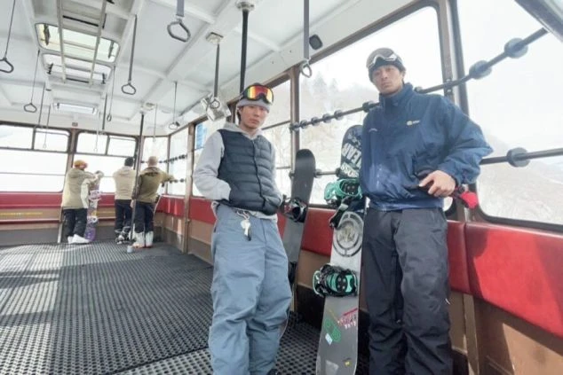ゴンドラの中でスノーボードを持った男性2人が立っている画像。リゾートバイトの休日に仲間とスノボを楽しむイメージ。