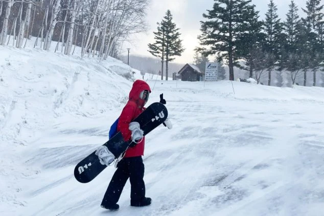 雪のゲレンデをスノーボードを持って歩く人物が映るイメージ画像。リゾートバイトの休日を満喫。