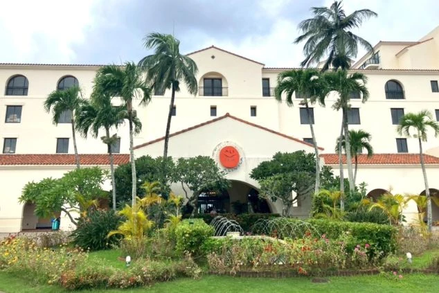 南国情緒あふれるヤシの木と花壇に囲まれた、スペイン風リゾートホテルの外観。