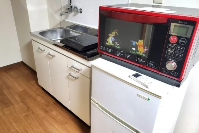 リゾートバイトの個室寮にあるミニキッチン。IHクッキングヒーター、シンク、電子レンジ、冷蔵庫が備え付けられた、自炊ができる便利な設備の画像。