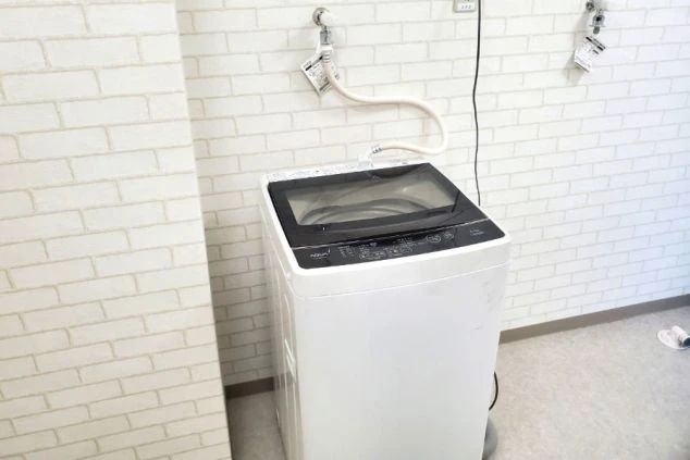 リゾートバイトの個室寮にある洗濯機。タイル張りの壁で清潔感があり、衣類の手入れに便利な設備の画像。