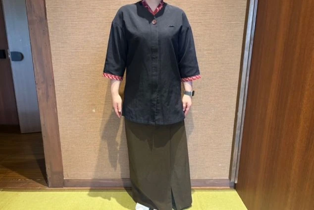 黒い上着にカーキ色のロングスカートを着用した女性スタッフの画像。落ち着いた和風のデザインの旅館や和食レストランでのサービススタッフの制服画像。