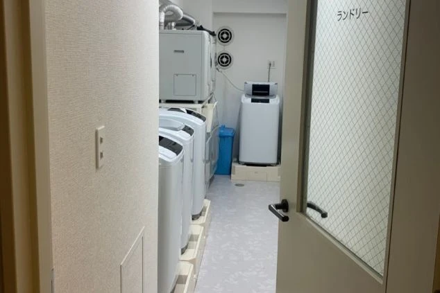 寮内のランドリールーム。複数台の全自動洗濯機と、棚に設置された衣類乾燥機が完備されています。