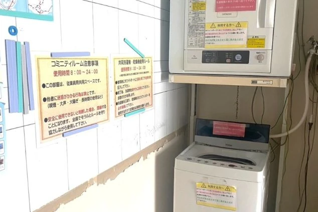 リゾートバイトの寮に設置された共用洗濯機と乾燥機。壁には利用時間や注意事項が書かれた掲示があり、規則を守って快適に利用できる設備の寮画像。